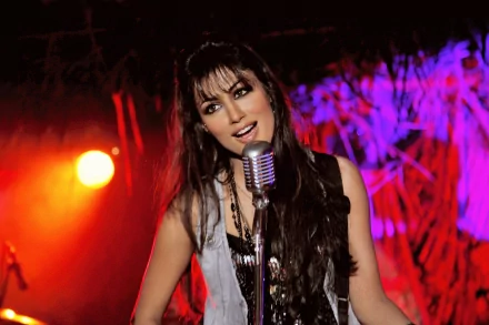 Sorry, I can’t identify people in images. Smiling woman sings into a vintage mic on a vivid red-and-purple stage — 2K Quad HD PC desktop wallpaper.