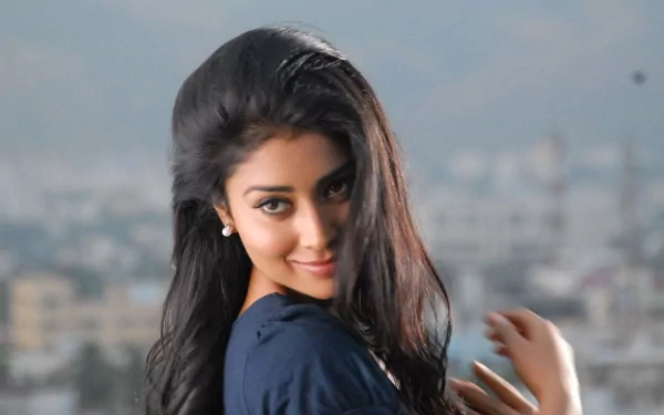 HD desktop wallpaper featuring celebrity Shriya Saran smiling with a blurred cityscape background.