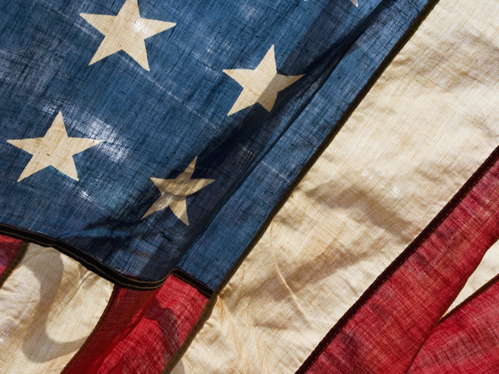HD desktop wallpaper featuring a close-up of a man-made American flag with visible fabric texture and weathered stars and stripes.