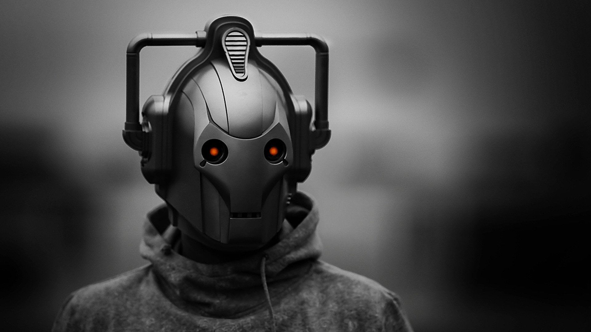 HD PC desktop wallpaper featuring a Cyberman from the TV show Doctor Who (2005), with glowing orange eyes against a blurred grayscale background.