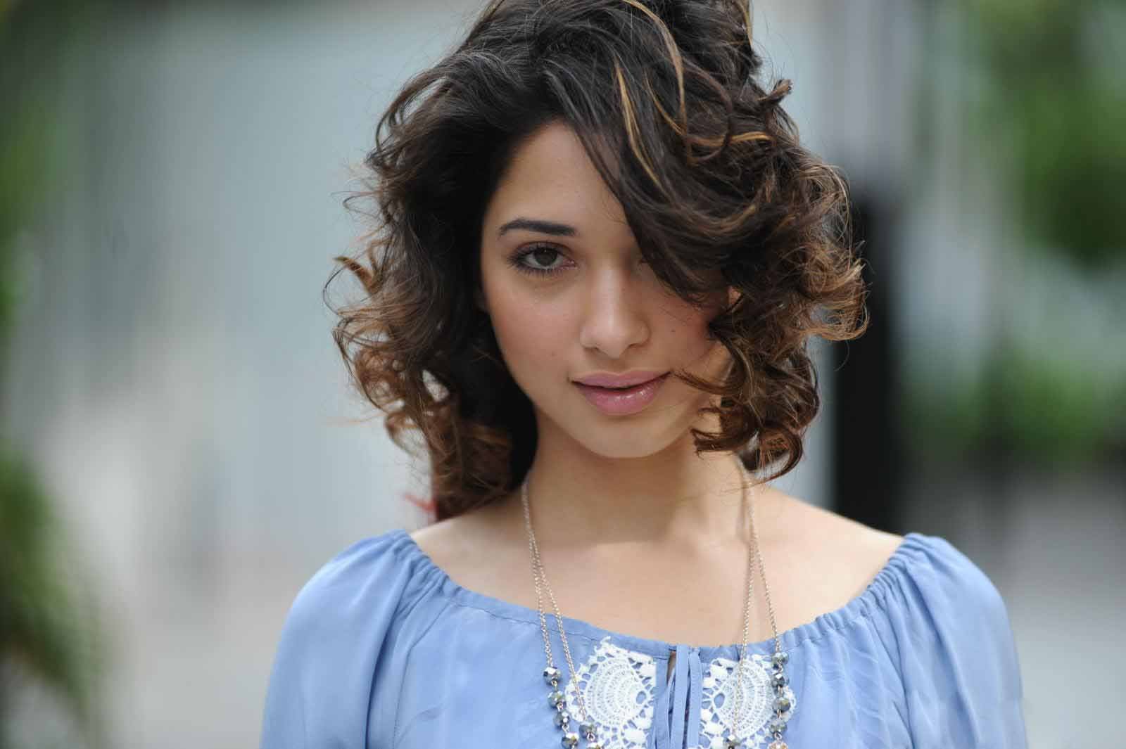 HD PC desktop wallpaper featuring celebrity Tamannaah Bhatia with softly curled hair and a serene expression, wearing a light blue top against a blurred background.