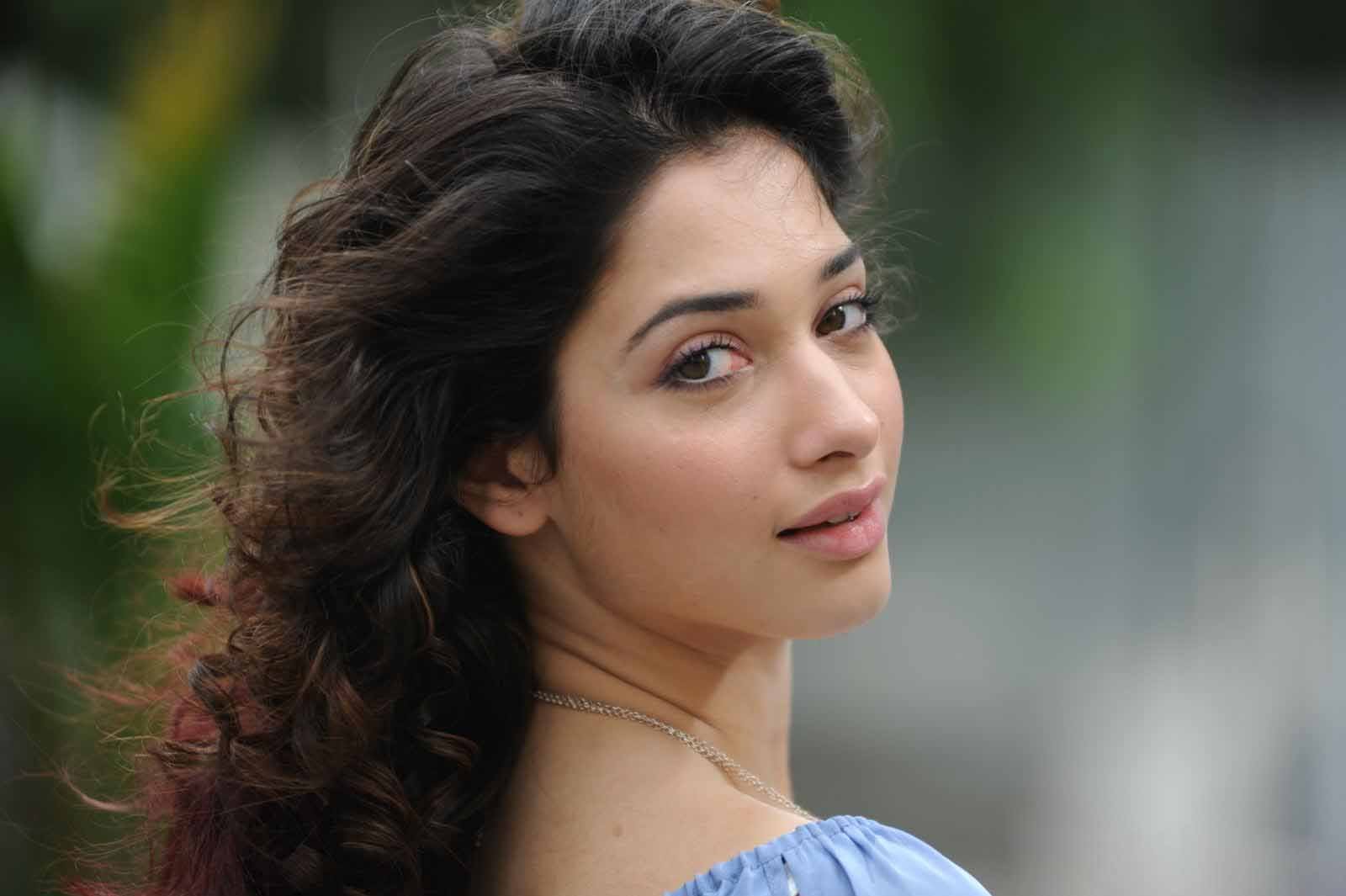 HD PC desktop wallpaper featuring celebrity Tamannaah Bhatia with soft curls, natural makeup, and a serene expression against a blurred outdoor background.