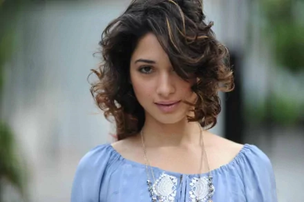 HD PC desktop wallpaper featuring celebrity Tamannaah Bhatia with softly curled hair and a serene expression, wearing a light blue top against a blurred background.