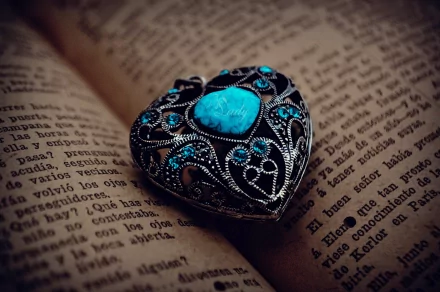 An HD desktop wallpaper featuring an intricately designed heart-shaped jewelry piece adorned with turquoise stones, resting on an open book with vintage-style text.