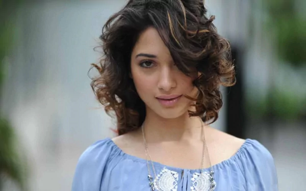 HD PC desktop wallpaper featuring celebrity Tamannaah Bhatia with softly curled hair and a serene expression, wearing a light blue top against a blurred background.