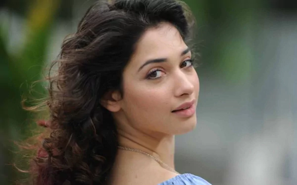 HD PC desktop wallpaper featuring celebrity Tamannaah Bhatia with soft curls, natural makeup, and a serene expression against a blurred outdoor background.