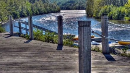 Scenic river view from a wooden dock surrounded by lush green trees, captured in vibrant detail as a 4K Ultra HD photography desktop wallpaper.