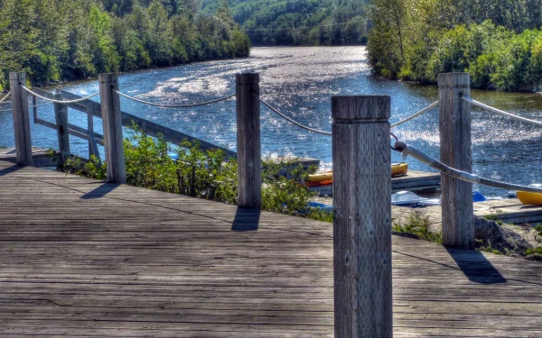 Scenic river view from a wooden dock surrounded by lush green trees, captured in vibrant detail as a 4K Ultra HD photography desktop wallpaper.