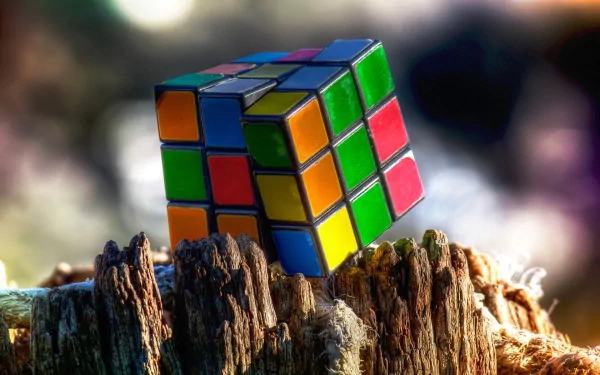 A colorful Rubik's Cube rests on a weathered tree stump, captured in sharp detail against a blurred background. HD desktop wallpaper and background.