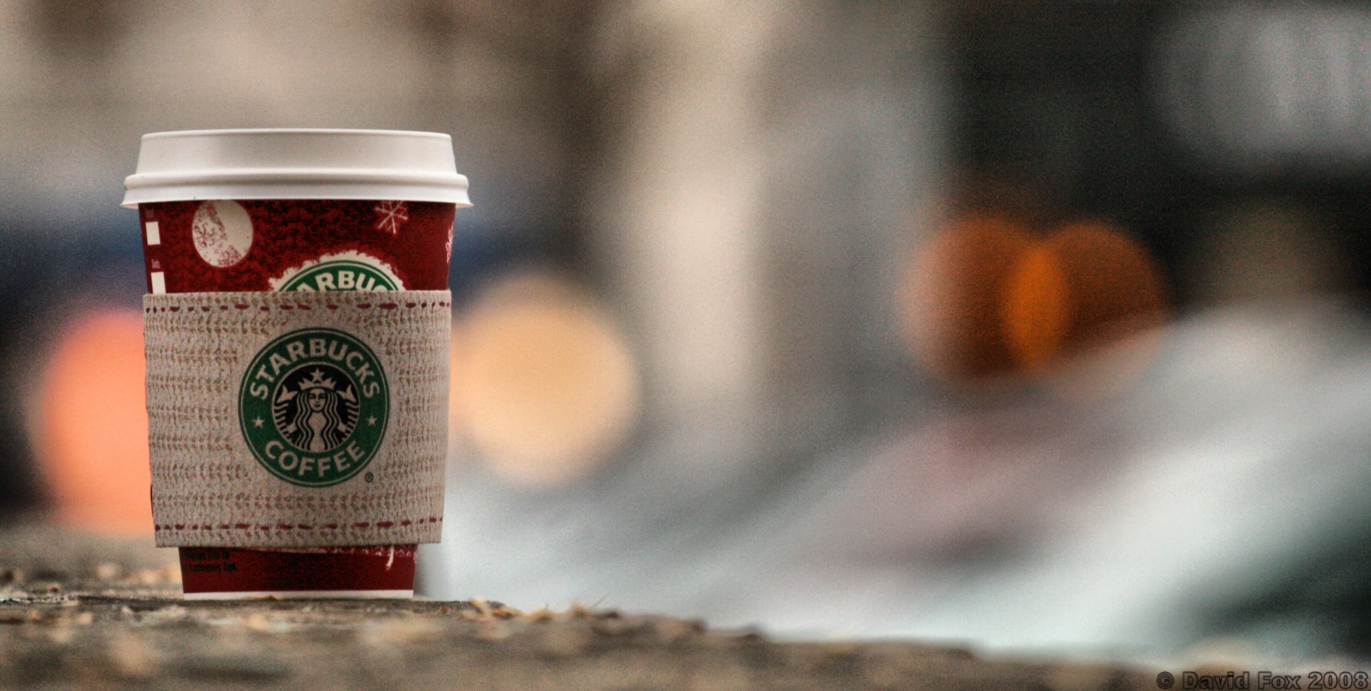 Close-up Starbucks takeaway coffee cup on a blurred city street; food and coffee themed 2K Quad HD PC desktop wallpaper/background.