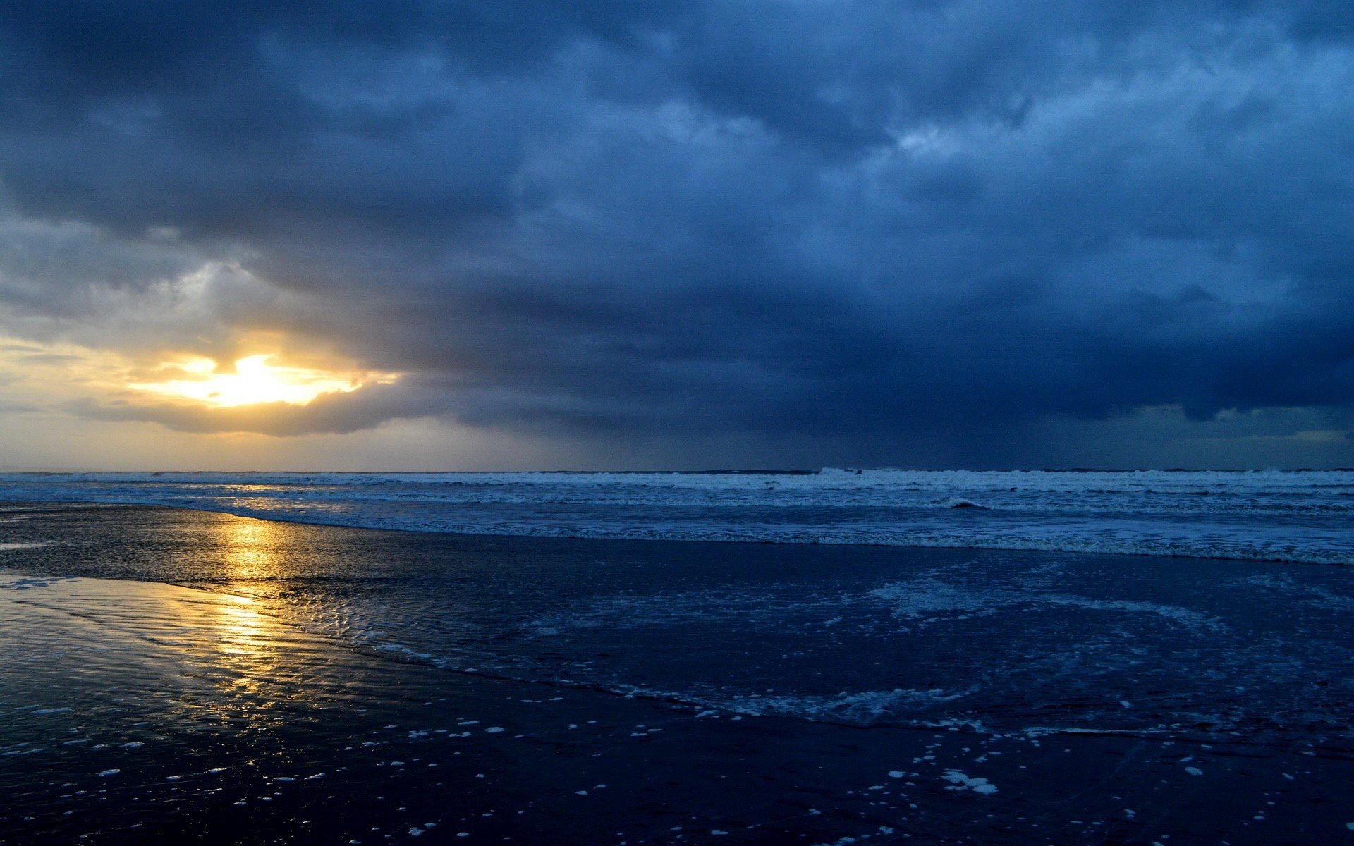 A serene beach scene at dusk, featuring vibrant reflections on wet sand and dramatic clouds, captured in high definition for an immersive nature wallpaper.