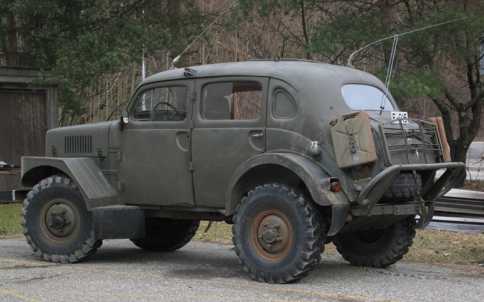HD PC desktop wallpaper showing a vintage military vehicle with rugged tires, weathered green paint, and equipment mounted on the rear, set against a wooded background.