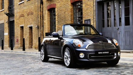 A sleek Mini Cooper convertible parked on a cobblestone street, set against a backdrop of striking brick buildings, creating a dynamic and stylish desktop wallpaper.