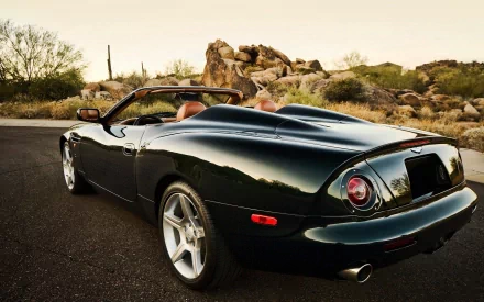 HD PC desktop wallpaper of a sleek black Aston Martin DB AR1 convertible parked on a desert road with rocky terrain in the background.