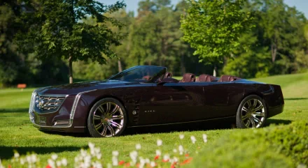 HD PC desktop wallpaper featuring a sleek, dark-colored Cadillac convertible parked on lush green grass with trees in the background.