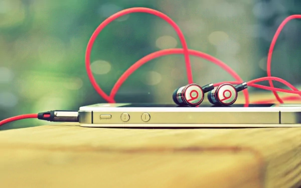 HD desktop wallpaper featuring a close-up of an iPhone with red Beats earphones resting on a wooden surface, highlighting technology and modern design.