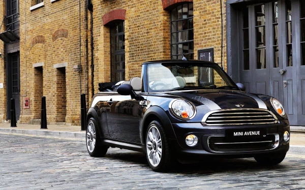 A sleek Mini Cooper convertible parked on a cobblestone street, set against a backdrop of striking brick buildings, creating a dynamic and stylish desktop wallpaper.