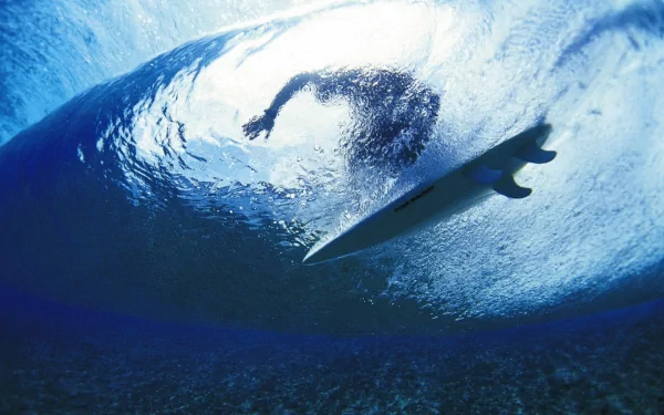 HD PC desktop wallpaper showing a surfer riding inside a large ocean wave, capturing the dynamic motion and energy of the sport of surfing.