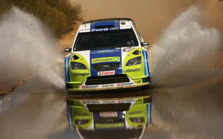 HD PC desktop wallpaper/background featuring a Ford Focus rally car splashing through water, frontal view with vivid yellow-green livery and mirrored reflection on the wet surface.