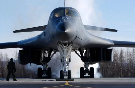 A powerful Rockwell B-1 Lancer military aircraft prepares for takeoff, exuding strength with smoke trailing from its engines, set against a clear background. HD desktop wallpaper.