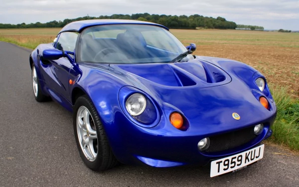 HD PC desktop wallpaper featuring a sleek blue Lotus sports car parked on a rural road with fields in the background.