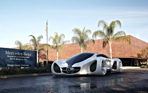 A sleek, futuristic Mercedes vehicle is parked near the Mercedes-Benz Research and Development facility in California, surrounded by palm trees, set against a clear blue sky.