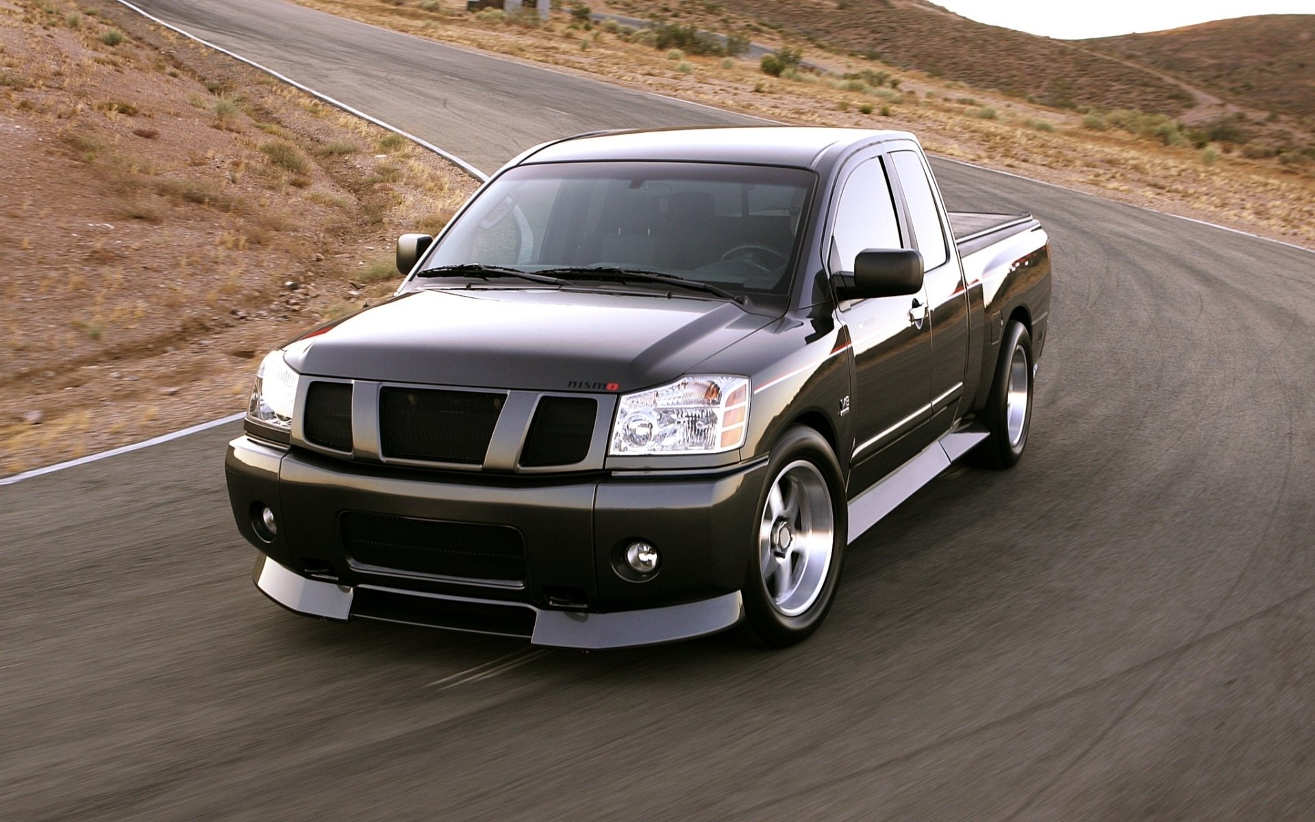 Black Nissan pickup truck driving on a winding desert road, captured as an HD PC desktop wallpaper and background.