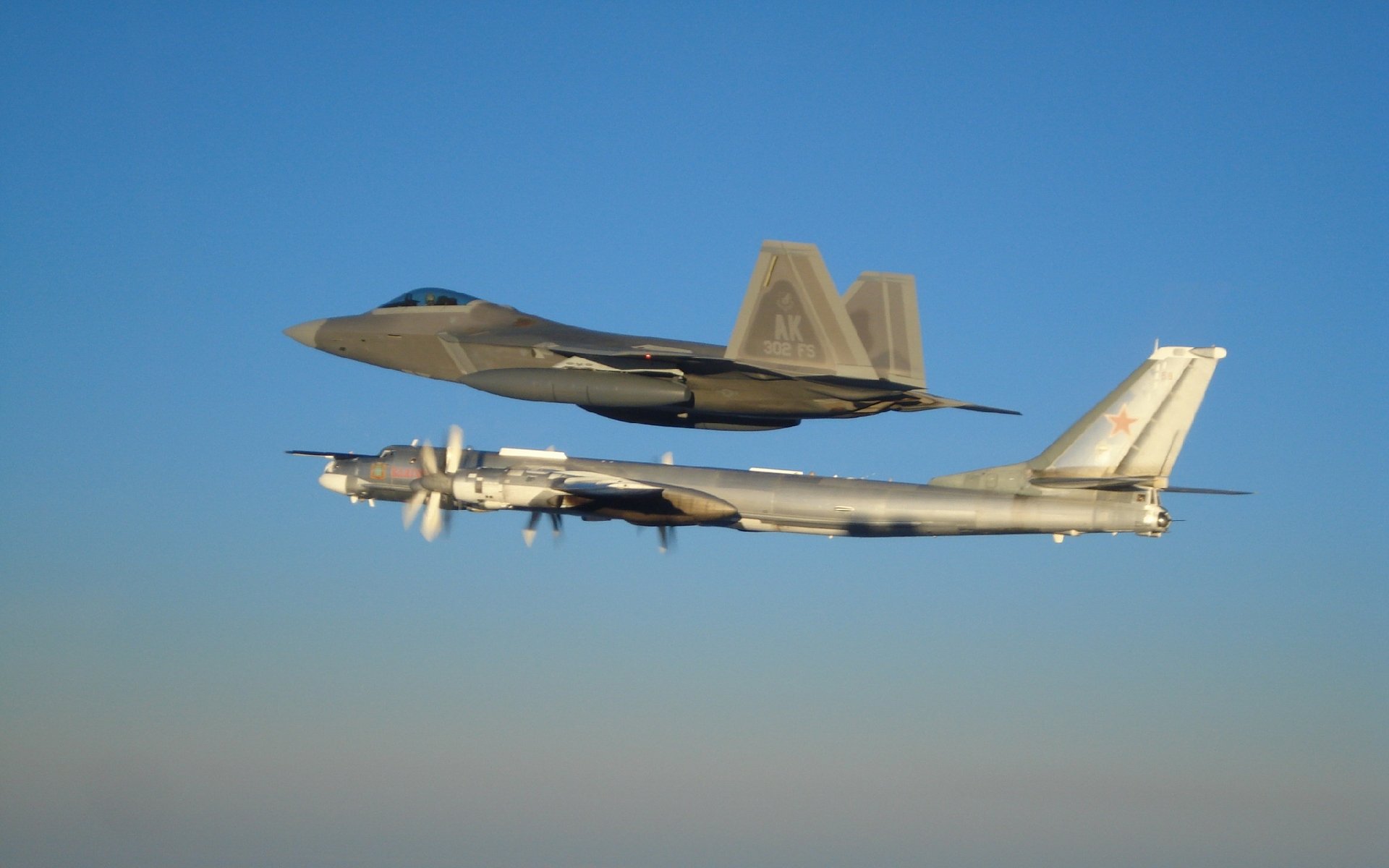 HD desktop wallpaper featuring two military aircraft flying side by side against a clear blue sky.