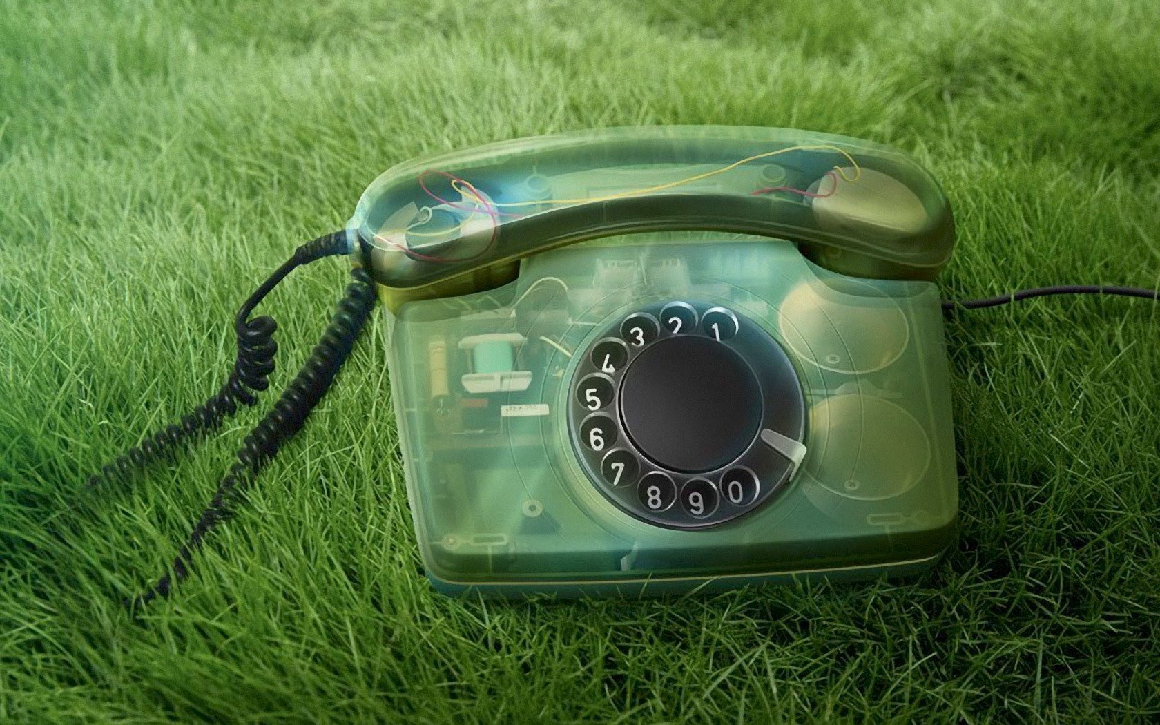 A vintage transparent rotary phone resting on green grass, captured in high definition as a PC desktop wallpaper background emphasizing technology and communication.