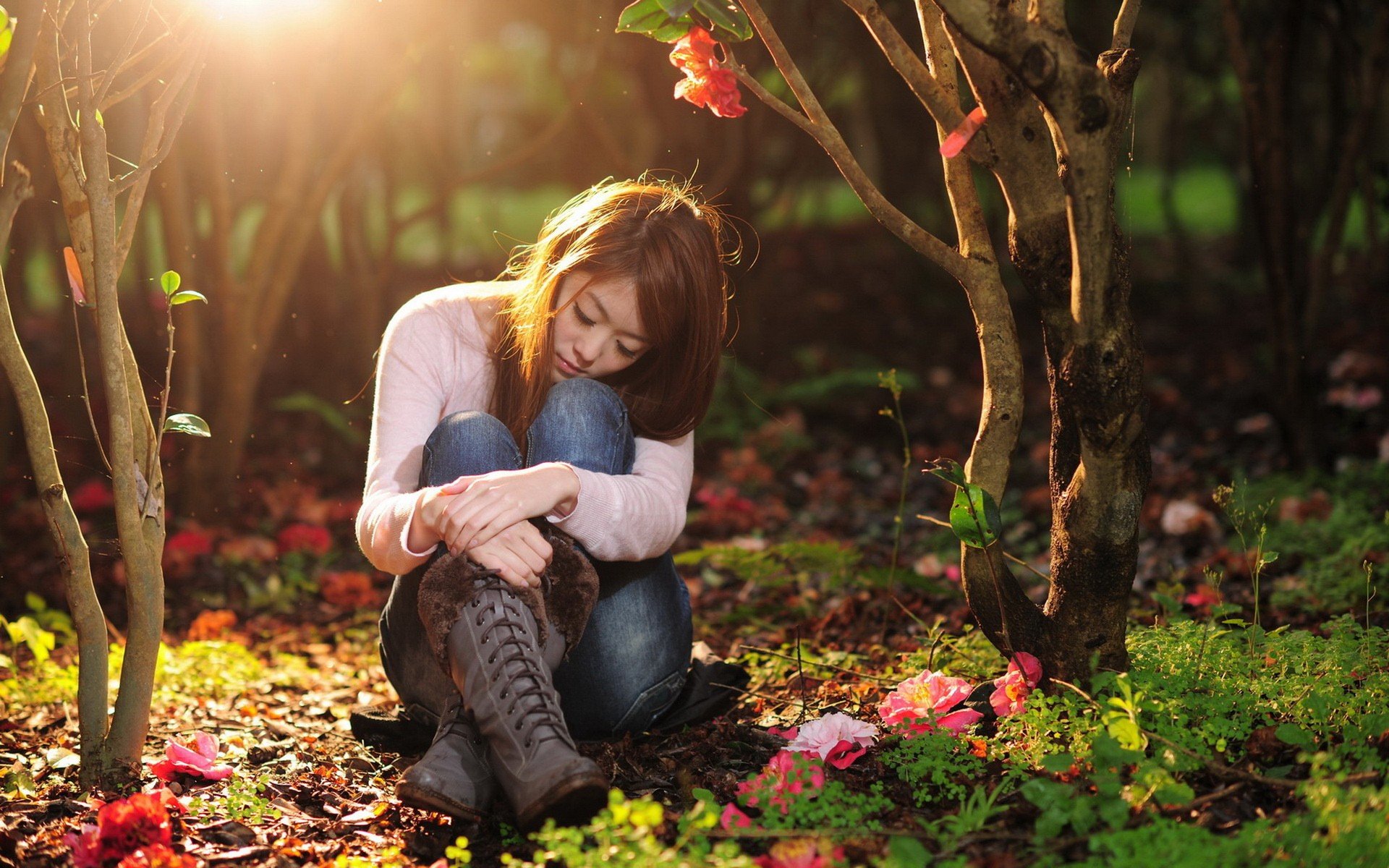 A serene woman sits among colorful flowers in a sunlit forest, reflecting a mood of tranquility. This HD desktop wallpaper and background captures a peaceful moment in nature.