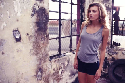 Unidentified woman in a gray tank top and black shorts standing by a distressed industrial wall; moody 2K Quad HD PC desktop wallpaper.