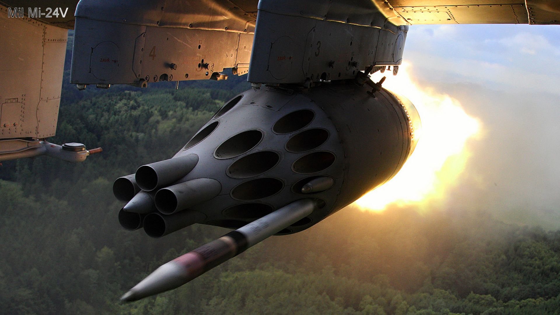 HD PC desktop wallpaper showing a close-up of a military rocket launcher firing rockets in mid-air with a forest visible below.