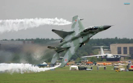 A Mikoyan MiG-29 fighter jet performs a dynamic maneuver, leaving trails of smoke against a backdrop of an airshow, showcasing military aviation prowess. HD desktop wallpaper.