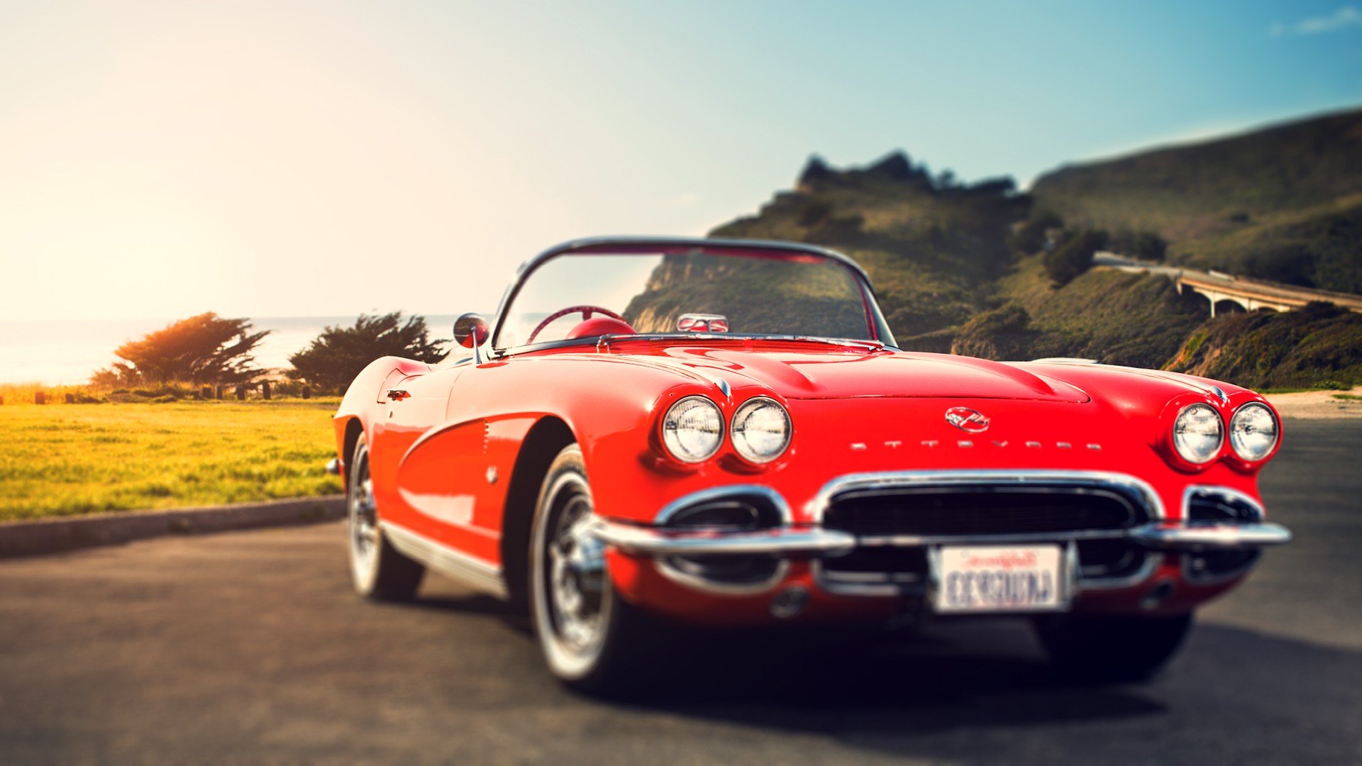 HD PC desktop wallpaper featuring a classic red Chevrolet convertible parked on a scenic road with mountains and a bright sky in the background.
