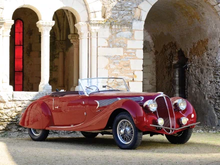 HD PC desktop wallpaper featuring a classic red Delahaye 135 vintage vehicle parked beside historic stone arches.