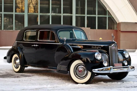 A black vintage Packard 180 full-size car parked in front of a large window, showcased as an HD PC desktop wallpaper and background.