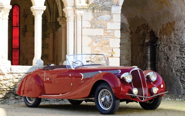 HD PC desktop wallpaper featuring a classic red Delahaye 135 vintage vehicle parked beside historic stone arches.