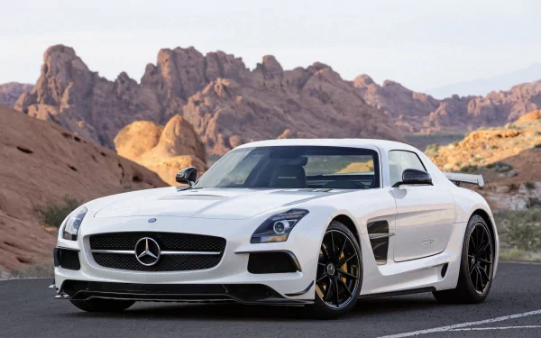 A sleek white Mercedes SLS AMG sports car parked on a road with dramatic rocky mountains in the background. This high-definition image serves as a stunning desktop wallpaper.