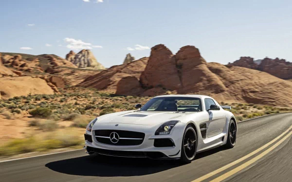 A sleek white Mercedes SLS AMG speeds along a winding road, framed by stunning rock formations and a clear blue sky, creating a striking HD desktop wallpaper.