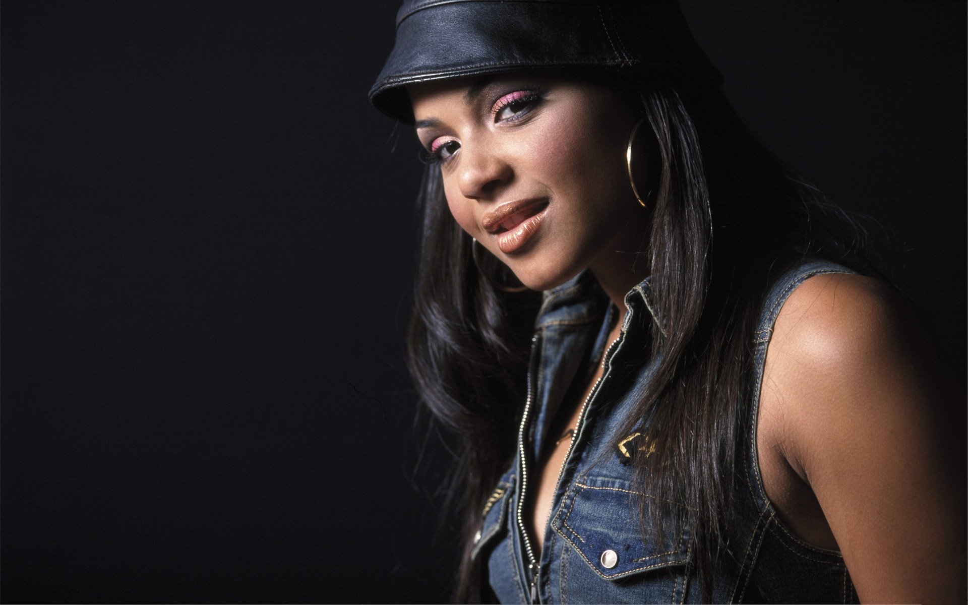 HD desktop wallpaper featuring Christina Milian in a dark setting, wearing a leather hat and denim vest, representing music and style.