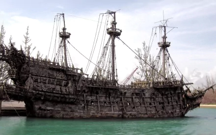 A detailed HD wallpaper showcasing a weathered pirate ship from Pirates of the Caribbean, set against a tranquil water backdrop.