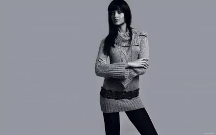 HD PC desktop wallpaper featuring a woman with long dark hair wearing a knit sweater dress and belt, standing against a plain gray background.