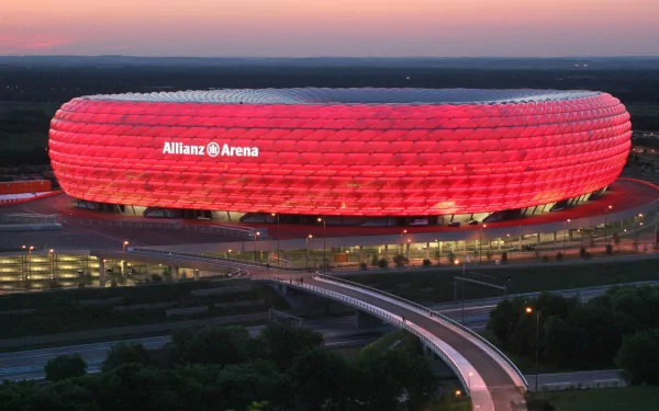 Aerial view of Allianz Arena illuminated in red at dusk, showcasing its modern architecture in a high-definition sports stadium wallpaper.
