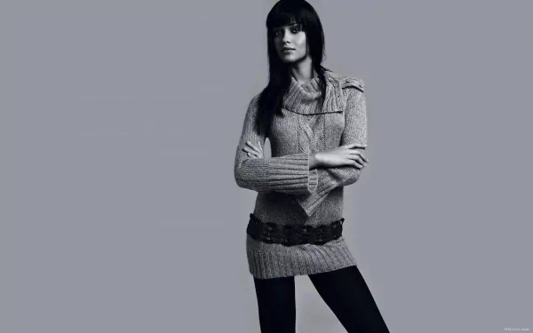 HD PC desktop wallpaper featuring a woman with long dark hair wearing a knit sweater dress and belt, standing against a plain gray background.