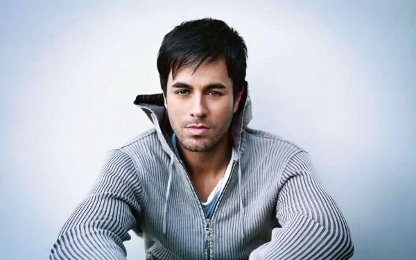 HD desktop wallpaper of Enrique Iglesias, tagged with music. He is wearing a gray zip-up sweater and looking directly at the camera against a light blue background.