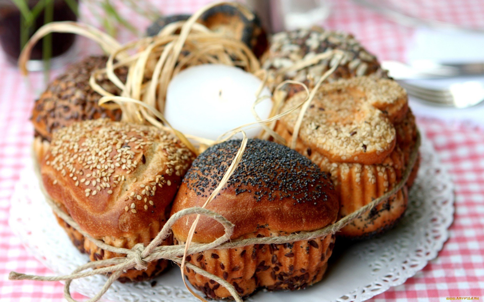HD PC desktop wallpaper showing a rustic assortment of seeded bread rolls arranged in a circular pattern with a candle tied in the center on a lace doily.