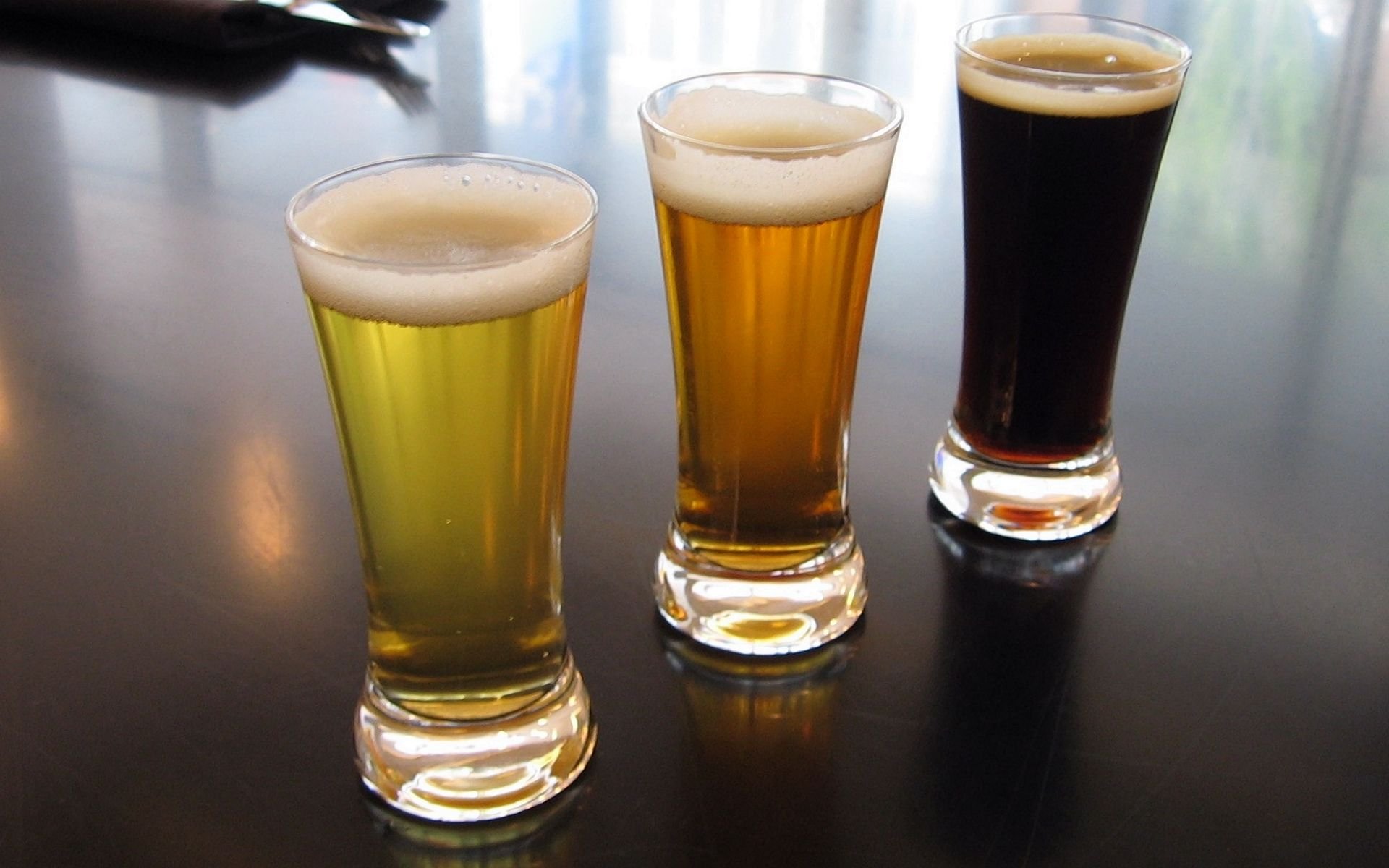 HD PC desktop wallpaper showing three glasses of beer in varying colors on a dark reflective surface, featuring food and beer themes.