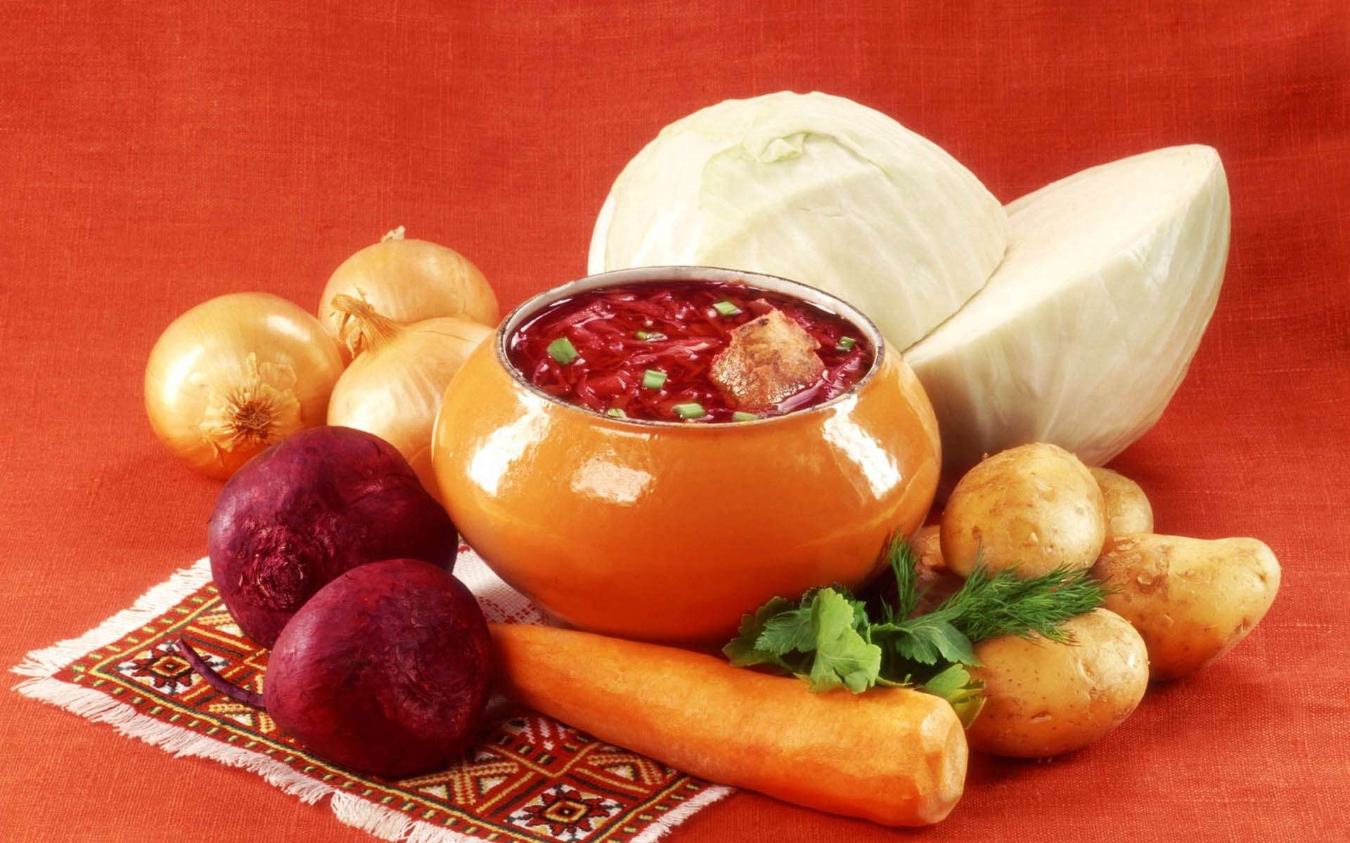 HD PC desktop wallpaper featuring a vibrant bowl of soup surrounded by fresh vegetables on a patterned cloth against a warm orange background.