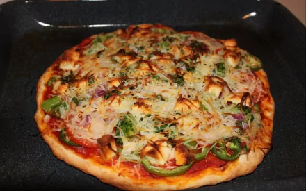 HD desktop wallpaper showing a freshly baked pizza topped with cheese, green peppers, and onions on a dark baking tray.