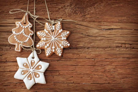 A festive display of gingerbread cookies shaped like a Christmas tree and snowflakes, adorned with white icing, set against a rustic wooden background.